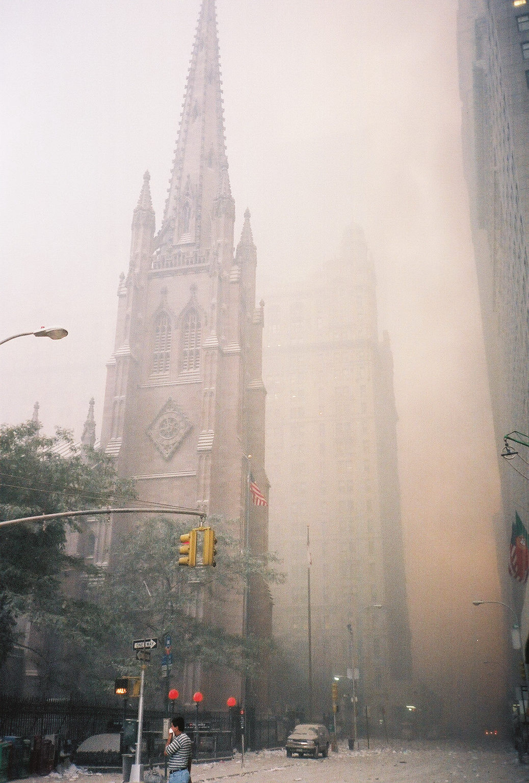Trinity Church surrounded by dust and debris but undamaged; the red glow of fire from the collapsed buildings north up Broadway.
