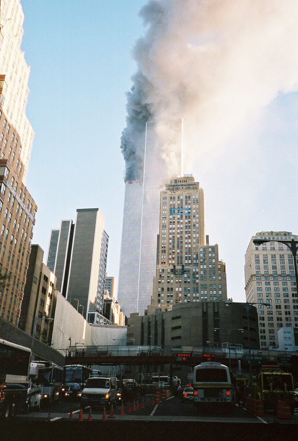 Seconds later - the smoke turning grey, the North Tower aflame with black smoke, a large gash visible in the South Tower.